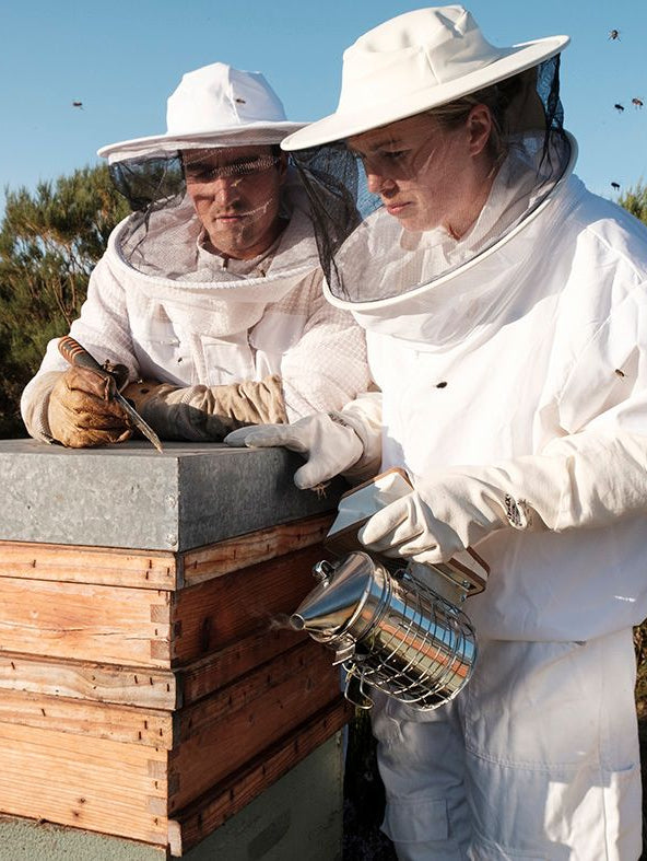 Billede af en mand og dame i hvide dragter, foran en bistade, fra Olaya i Spanien.