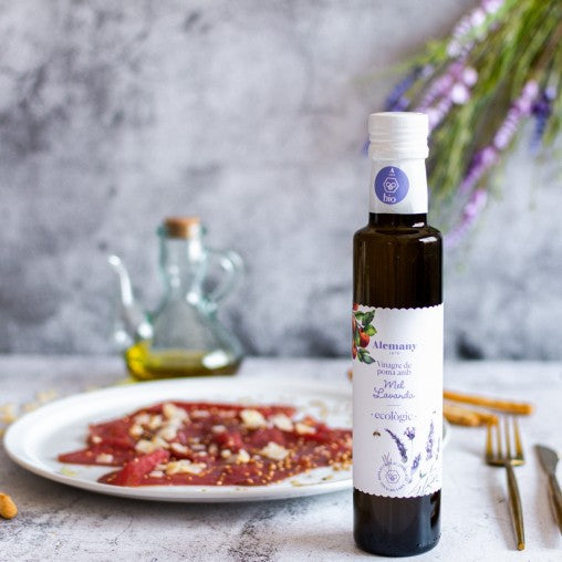 Flaske med Æblecidereddike med økologisk lavendelhonning fra Alemany på dækket bord med carpaccio på tallerken.