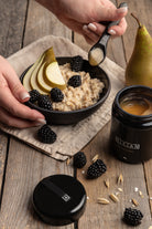 sjælden og exceptionel Hikiän – finsk honning i sin reneste form, i ekslusiv sort glas, på et bord med morgengrød med pærer og brombær. 