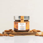 Glas Alemany mandelcreme  med honning og kakao , omkranset af mandler på et bord.